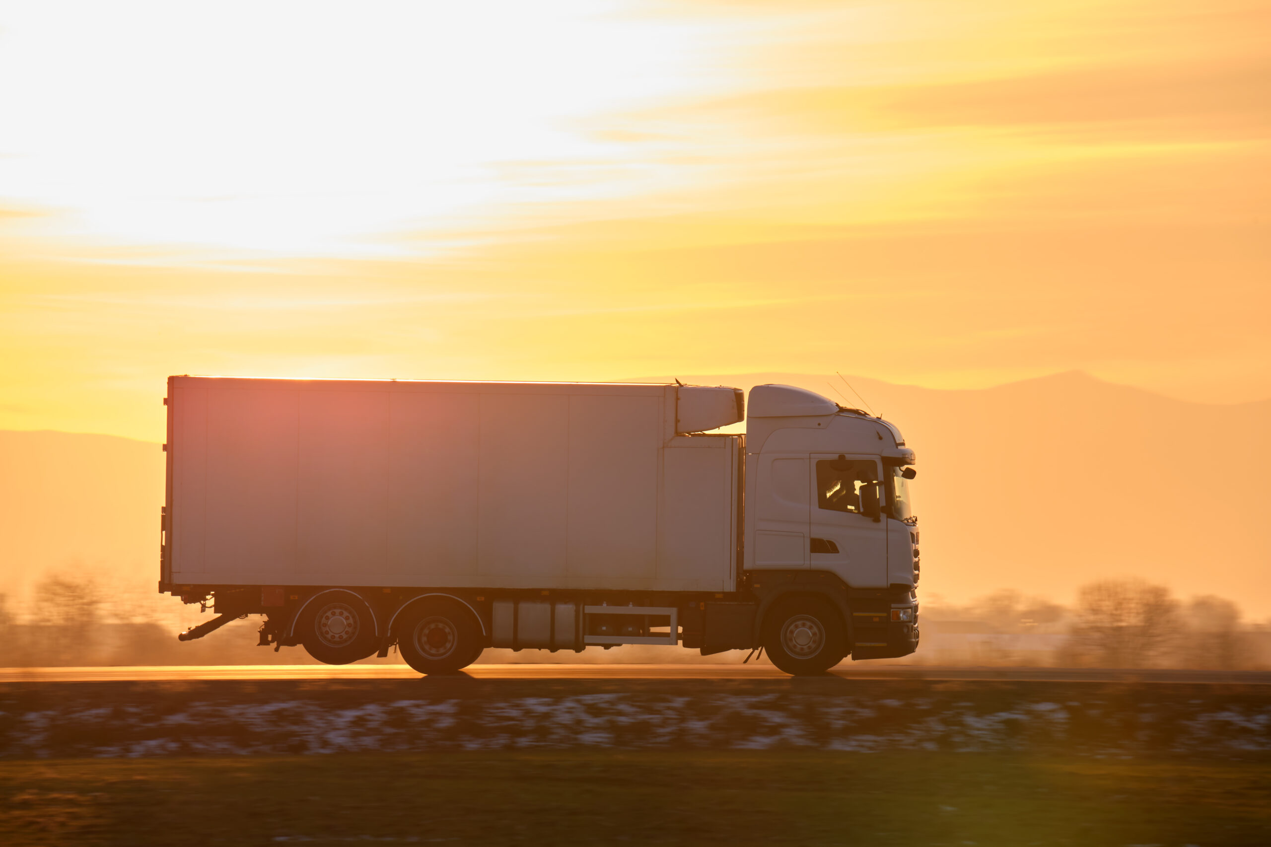 Cargo truck driving on highway hauling goods in evening. Delivery transportation and logistics concept.